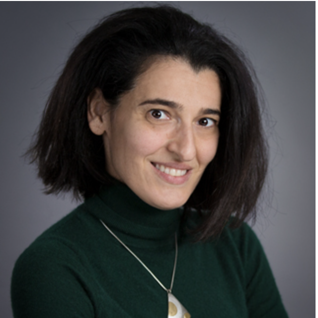 A woman in a dark green turtleneck and shoulder-length black hair smiles at the camera.